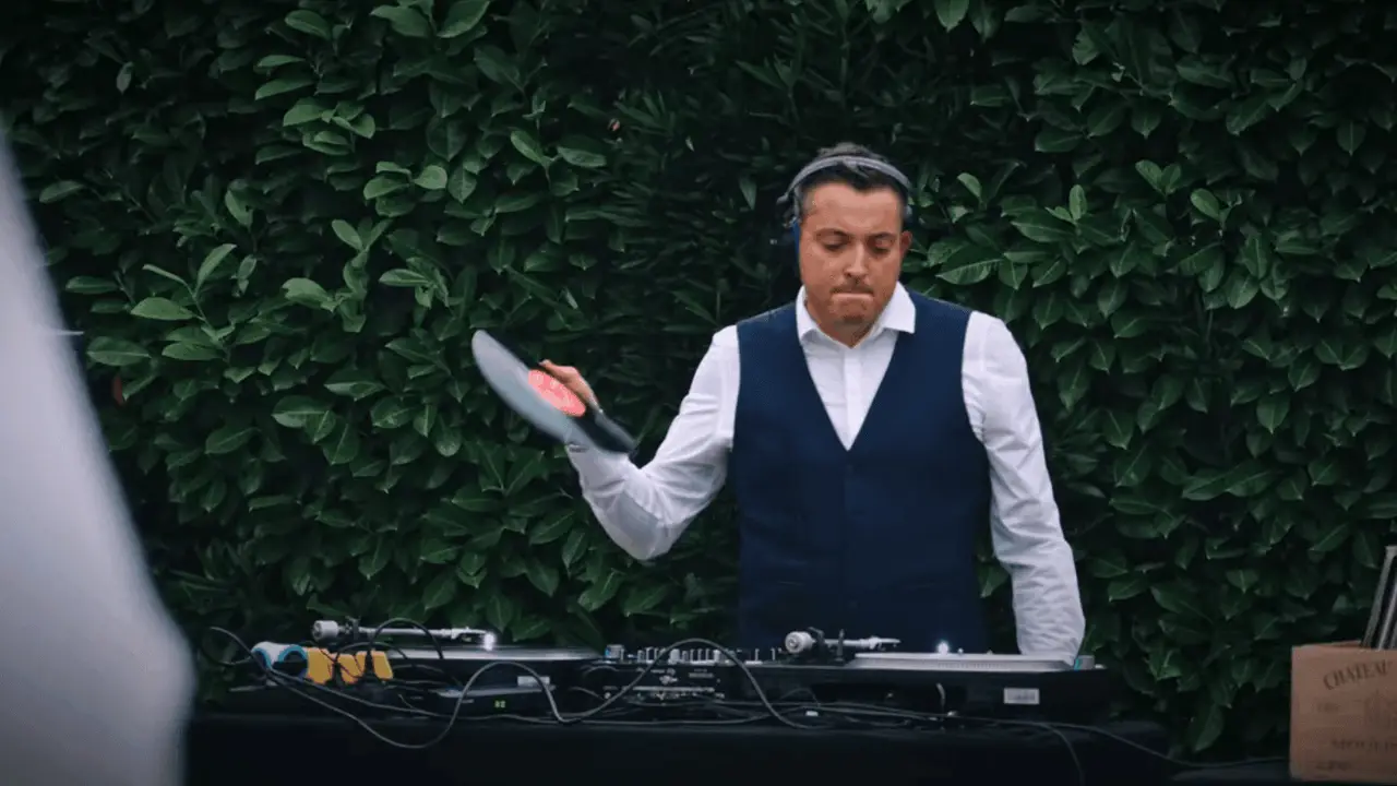 Tom Emersson mixant sur platines vinyles devant une haie, lors d'un cocktail