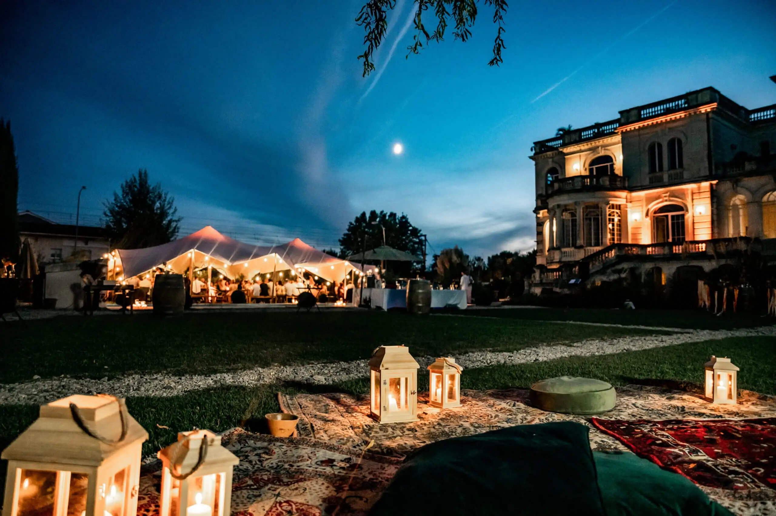 Chapiteau de réception éclairé de lanternes au crépuscule, devant un château