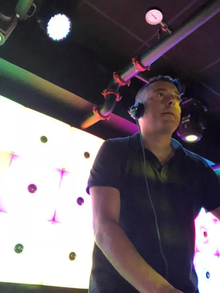 Tom Emersson aux platines devant un mur lumineux, casque autour du cou