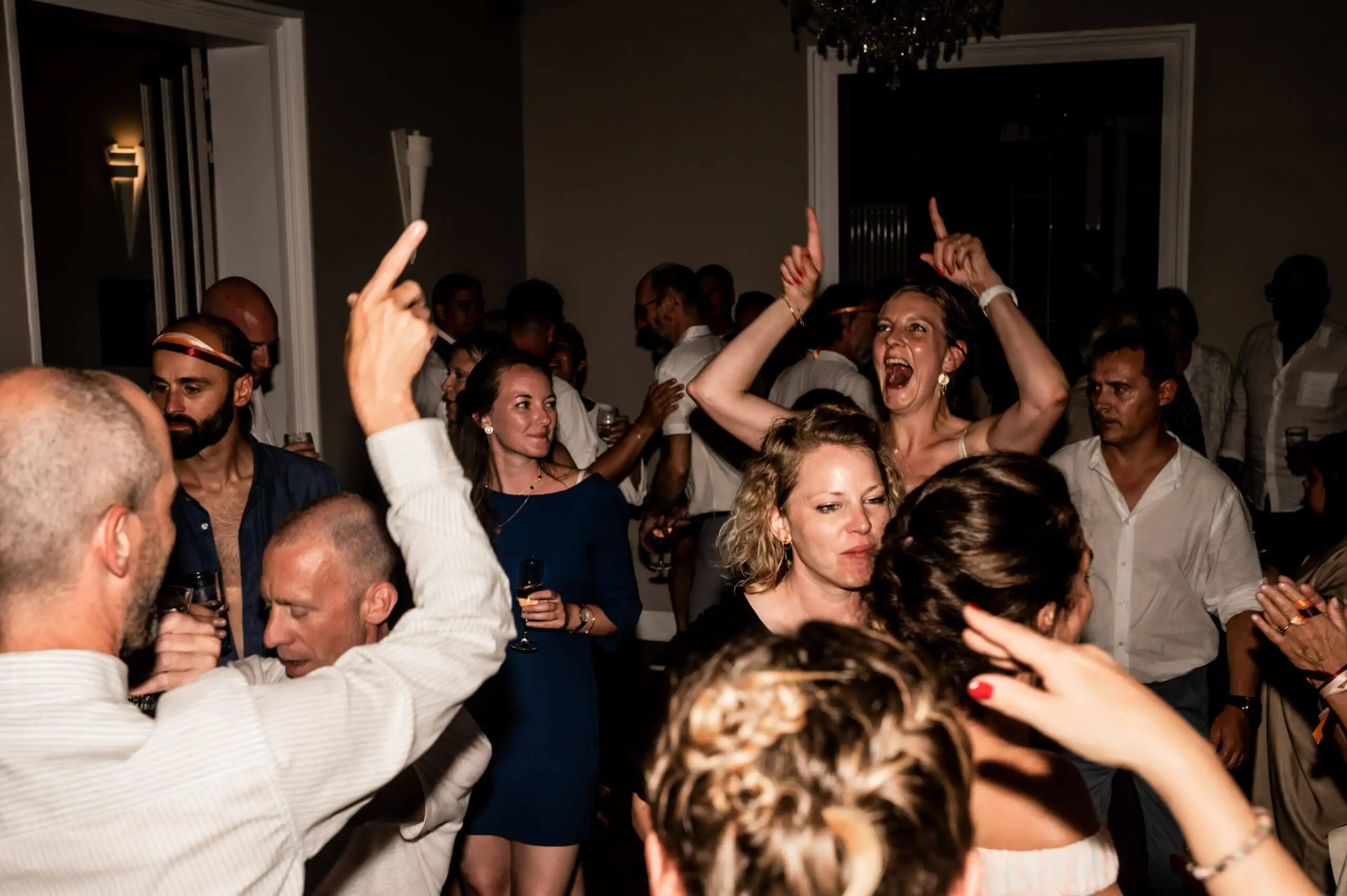 Invités serrés sur la piste, bras levés, en pleine soirée de mariage
