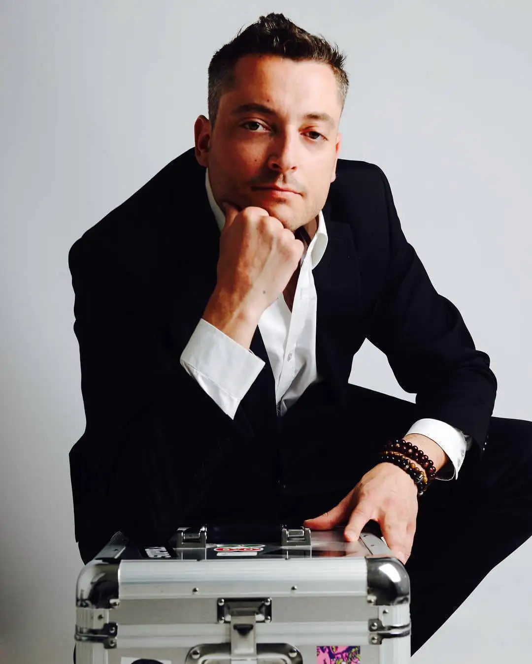 Portrait de Tom Emersson en costume, la main posée sur un flight case