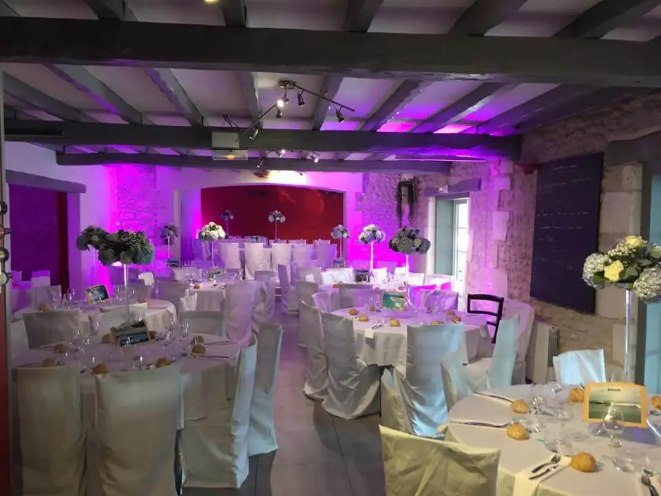 Salle de réception sous poutres, tables dressées et mise en lumière violette